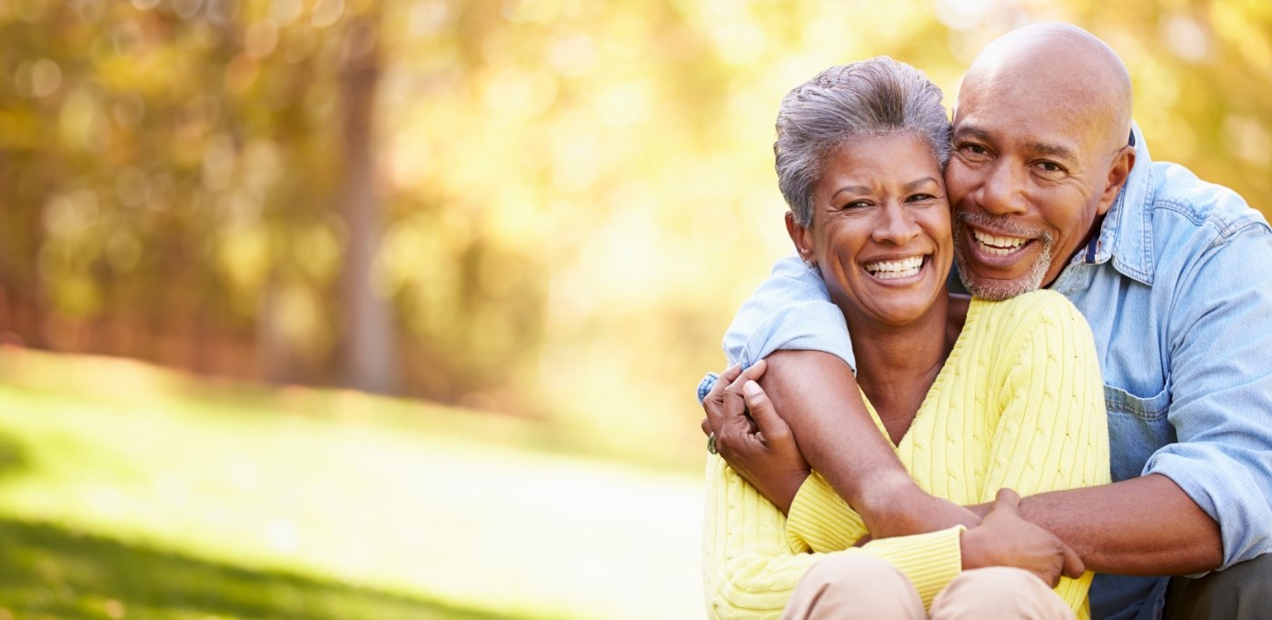 Senior couple hugging and smiling outdoors with All on 4 dental implants in Baytown