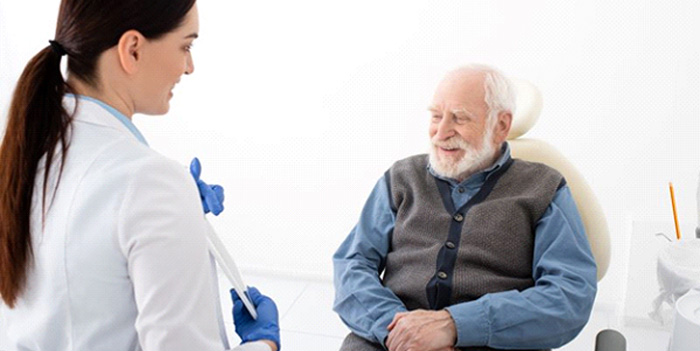 Senior man sitting in dental chair and talking to female dentist