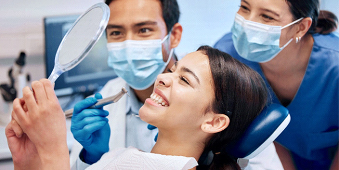 Two dentists watching patient check teeth in handheld mirror