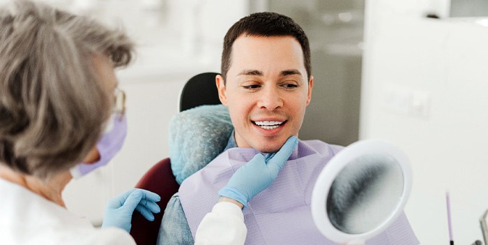 Man smiling at reflection in mirror with dentist