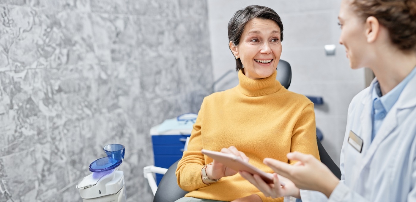 Senior woman in yellow sweater sitting in dental chair and talking to her dentist