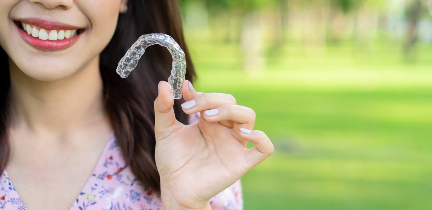 Smiling woman holding an Invisalign clear aligner